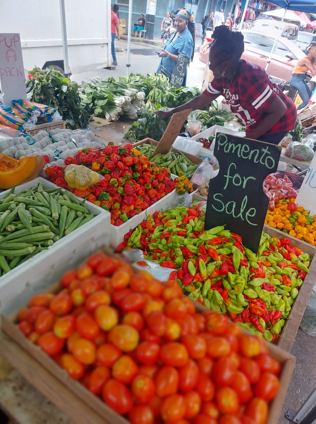 A Trinidad market stall with boxes of fresh pimento peppers beneath a hand-lettered 'Pimento for Sale' chalkboard sign